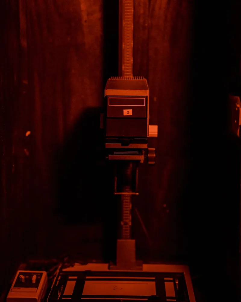 Ampliadora de laboratorio con el cabezal sobre el marginador, iluminada por la luz de seguridad roja del cuarto oscuro