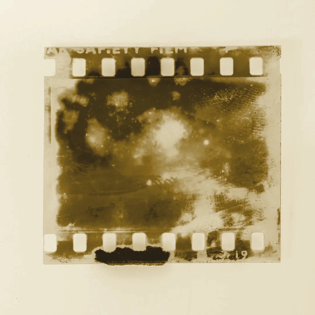 Fotograma de película de 35 mm en blanco y negro con manchas de revelado, apoyado sobre fondo claro